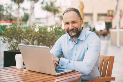 Portrait of businessman sitting with laptop at cafe