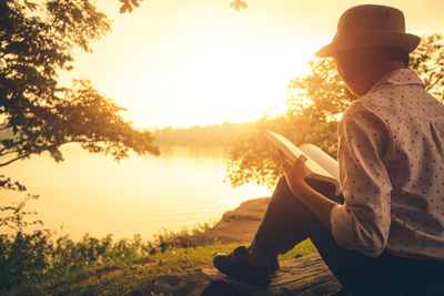 Man sitting by lake against sky during sunset