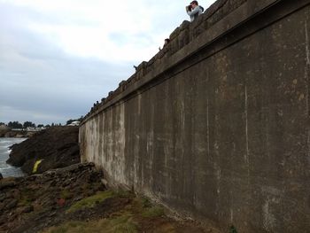 Low angle view of people on wall against sky