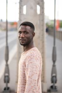 Portrait of young man looking away while standing on bridge