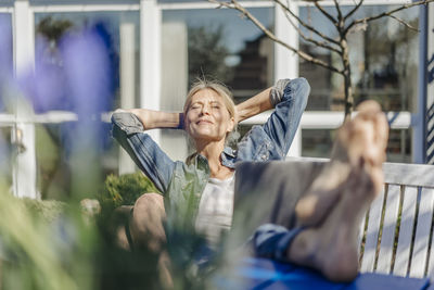 Smiling woman with laptop relaxing on garden bench