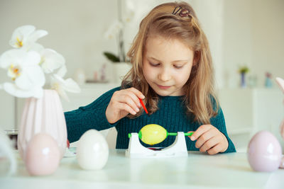 Cute girl painting easter egg while sitting at home