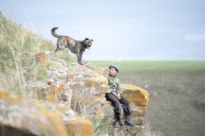 Man looking at dog while sitting on cliff at mountain