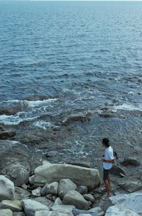 Rear view of boy standing on rock in sea