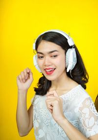 Portrait of smiling young woman against yellow wall