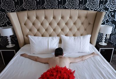 Rear view of shirtless man lying on bed