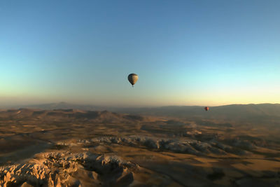 Hot air balloons flying over cappadocia against clear sky during sunset