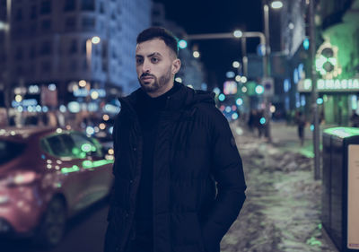 Portrait of young man standing in city at night