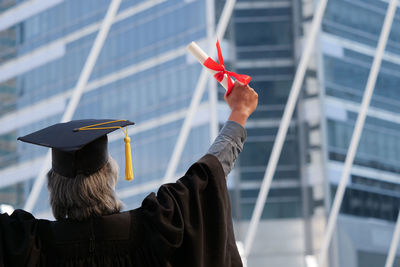 Rear view of man wearing graduation gown against building