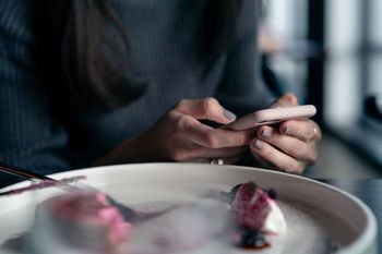 Midsection of woman using smart phone while eating meal