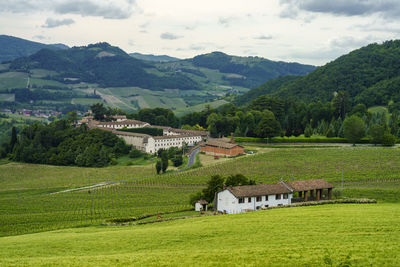 Houses and trees on field by mountains against sky