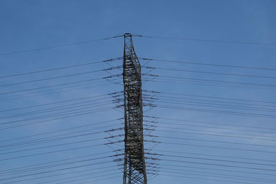 Low angle view of electricity pylon against blue sky