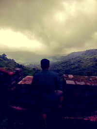 Rear view of man sitting on landscape against sky