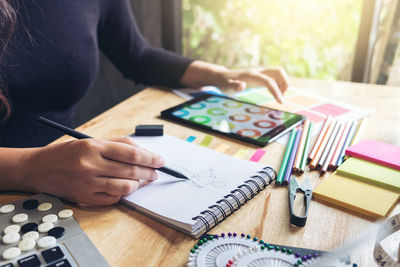 Midsection of fashion designer sketching on clipboard