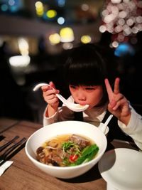 Girl showing peace sign while having soup at table in restaurant