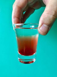 Close-up of hand holding drink against blue background