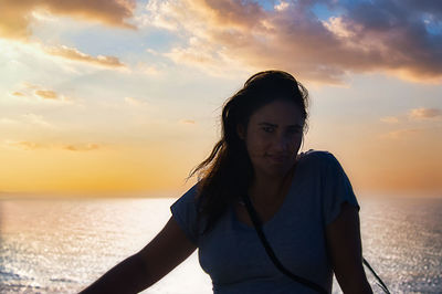 Young woman looking at sea against sky during sunset