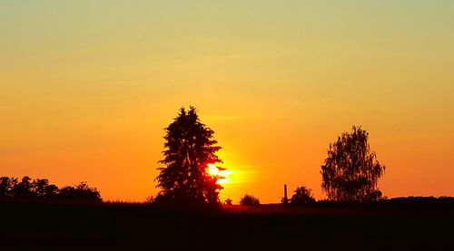 Silhouette trees on field against romantic sky at sunset