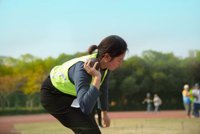 Side view of woman playing shot put at park against sky
