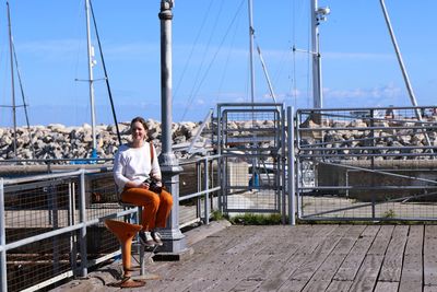 Full length of woman sitting by railing against sky