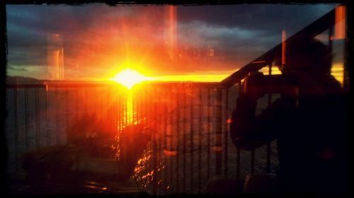 Silhouette person against sky during sunset seen through window