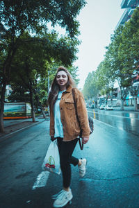 Portrait of smiling young woman standing on road in city