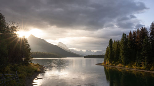 Sun rising on a cloudy sky above mountains and alpine lake , jasper n.park, canada