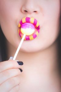 Cropped image of woman with yellow and pink lipstick eating lollipop