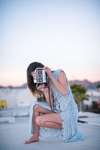 Portrait of woman photographing against sky during sunset