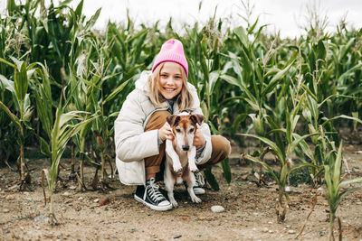 Happy teenage girl hugging her dog jack russell terrier in a field against a background