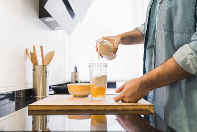Man cooking in the kitchen in a denim shirt. an anonymous man is pouring milk into a container