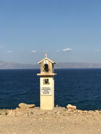 Information sign by sea against sky