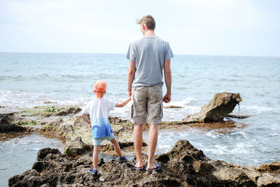 Rear view of father with son standing at beach against sky
