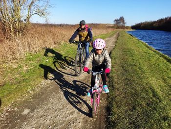 Full length of father and daughter riding bicycle on field