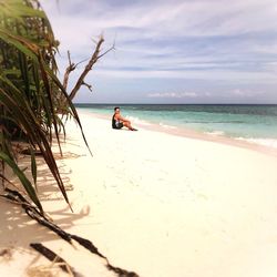 Man sitting on beach against sky