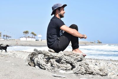 Full length of man sitting at beach against clear sky