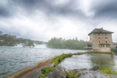 View of building by river against cloudy sky