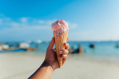 Cropped hand holding ice cream cone at beach