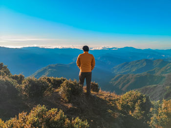 Rear view of man standing on mountain against sky