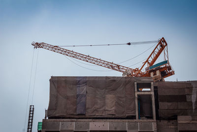 Low angle view of crane at construction site against sky