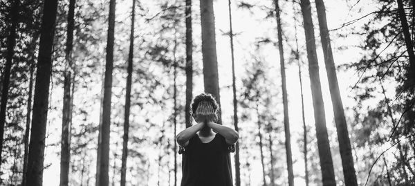 Rear view of woman standing amidst trees in forest