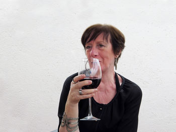Woman holding wineglass while sitting against wall