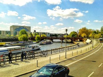 Cars on road by river in city against sky