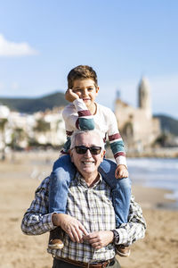 Portrait of grandfather piggybacking son at beach