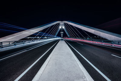 Light trails on bridge in city against sky at night