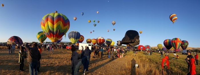 People looking at hot air balloons against sky