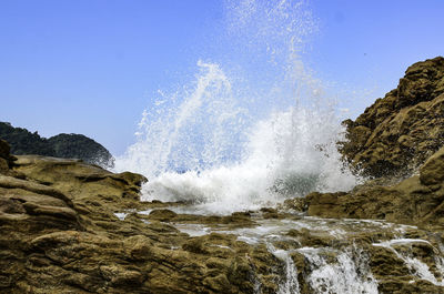 Waves splashing on rocks against clear sky