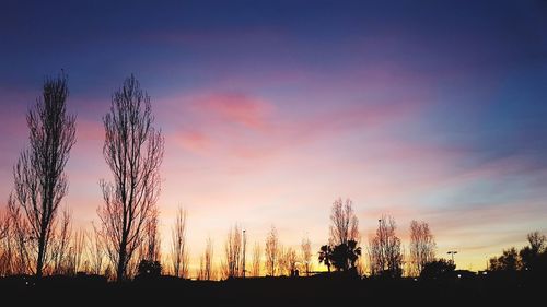 Silhouette trees on field against romantic sky at sunset