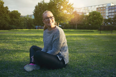 Portrait of smiling woman sitting on field in park during sunset