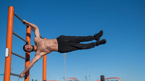 Low angle view of man exercising against clear blue sky